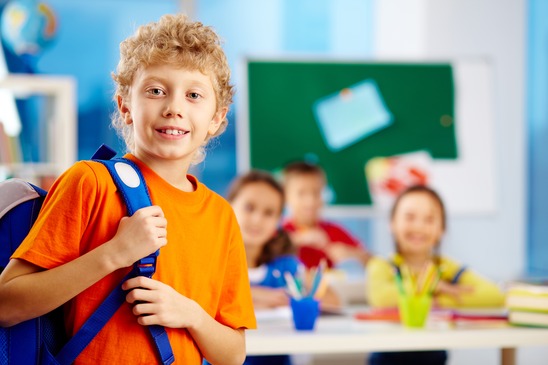 Portrait of cute schoolboy with backpack looking at camera with his classmates on background